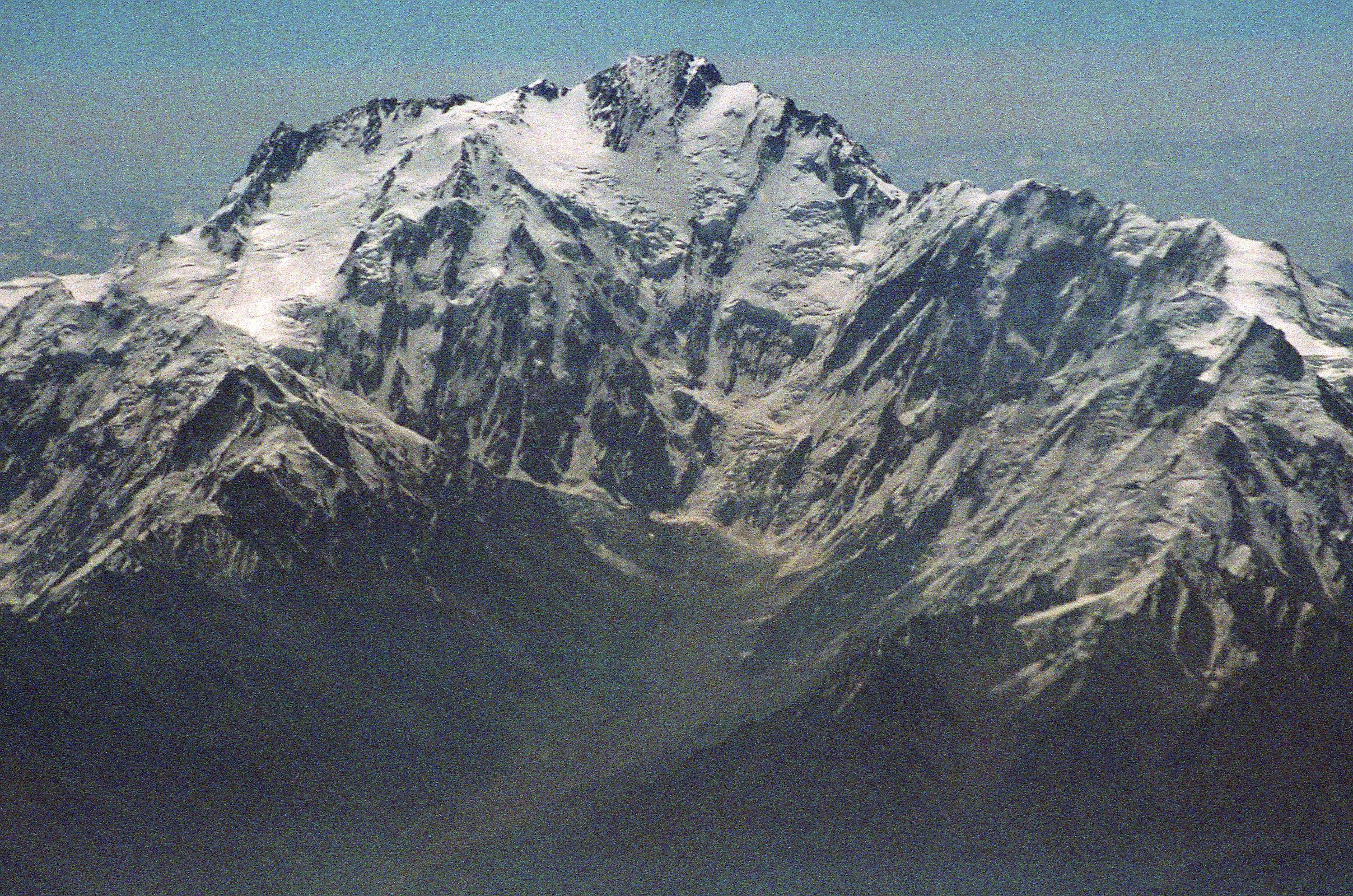 06 Nanga Parbat Diamir Face And Mazeno Ridge On Flight From Islamabad To Skardu On the 40-minute flight from Islamabad to Skardu, the captain announces, We'll be flying at a planned altitude of 8,000 metres. Perfect I thought, we'll be exactly at the height of Nanga Parbat. The flight starts low key with the stewardesses serving drinks while we bide our time. When the pilot announces Nanga Parbat is immediately ahead on the right, all hell breaks loose. As one, all the tourists, including me, are up in the aisles, craning their necks, running for the cockpit. The sounds of cameras are everywhere. There it is, within arms reach. Nanga Parbat in perfect early morning splendor! We are passing by the Diamir Face, as I click photo after photo. The massive Mazeno Ridge runs down to the right of Nanga Parbat. The Mazeno ridge is the longest ridge on any 8000m mountain and includes eight 7000m peaks. Nobody has managed to traverse the ridge and continue to the summit of Nanga Parbat.